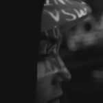 Artistic black and white close-up of an anonymous hacker with projected text, highlighting cyber security themes.